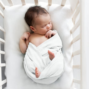 A newborn baby is peacefully sleeping in a white crib, swaddled in a soft blanket.