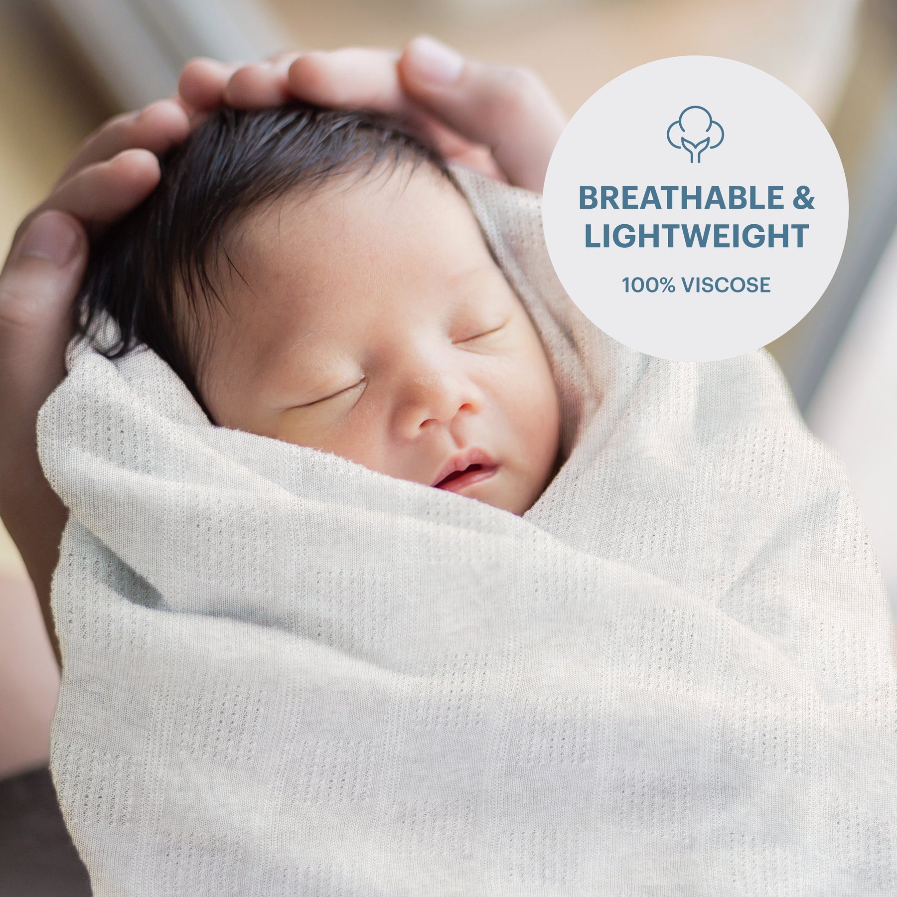 A newborn baby is swaddled in a white blanket, with hands gently cradling the baby's head.