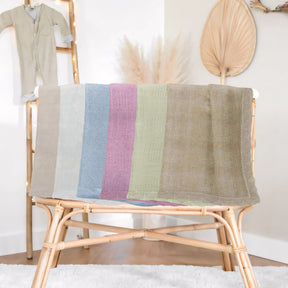 a wooden chair with a colorful striped blanket draped over it, placed in a room with a baby changing station and a decorative wall hanging.