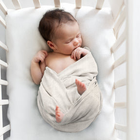 A newborn baby is peacefully sleeping in a white crib, swaddled in a soft blanket.