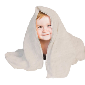 A young child with a smile on their face is partially hidden behind a white, patterned blanket.