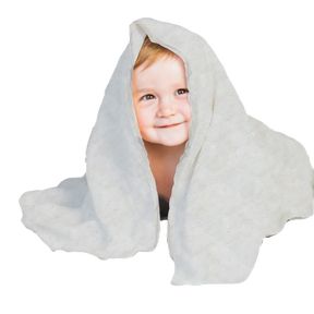 A young child with a smile on their face is peeking out from behind a white, polka-dotted blanket.