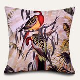 A decorative pillow with a vibrant, colorful illustration of two parrots perched on branches amidst tropical foliage.