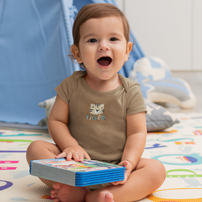 A smiling baby boy sitting on the floor, holding a book and looking at the camera.