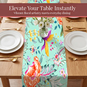 a table setting with a floral table runner, white plates, and gold cutlery.