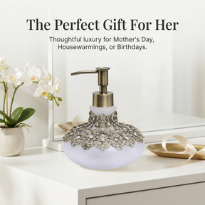 a decorative soap dispenser with a white and gold floral design, placed on a white countertop next to a vase of white flowers and a gold tray.