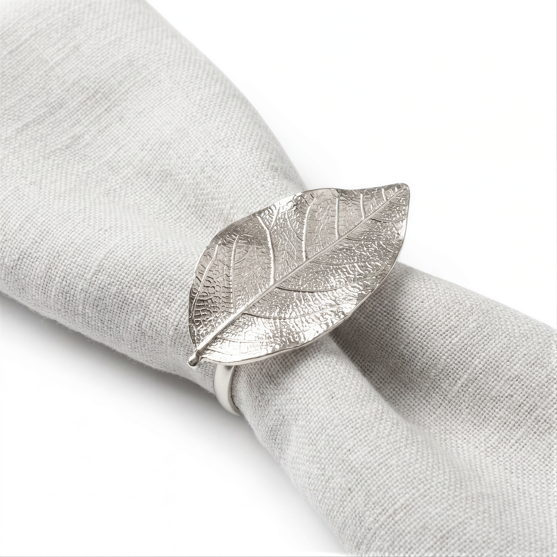 A silver metal napkin ring with a leaf-shaped design is placed on a white napkin.