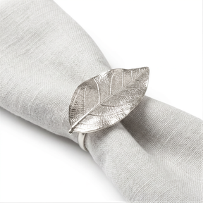 A silver metal napkin ring with a leaf-shaped design is placed on a white napkin.