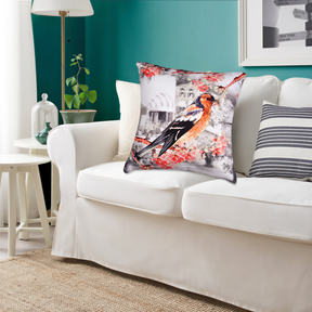 a living room with a white sofa, a decorative pillow with a bird design, and a small table with a plant and a lamp.