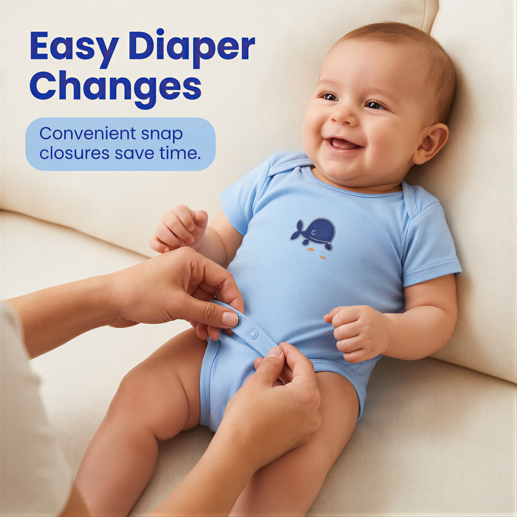 A smiling baby wearing a blue onesie with a whale design, being fastened into a diaper by someone's hands.