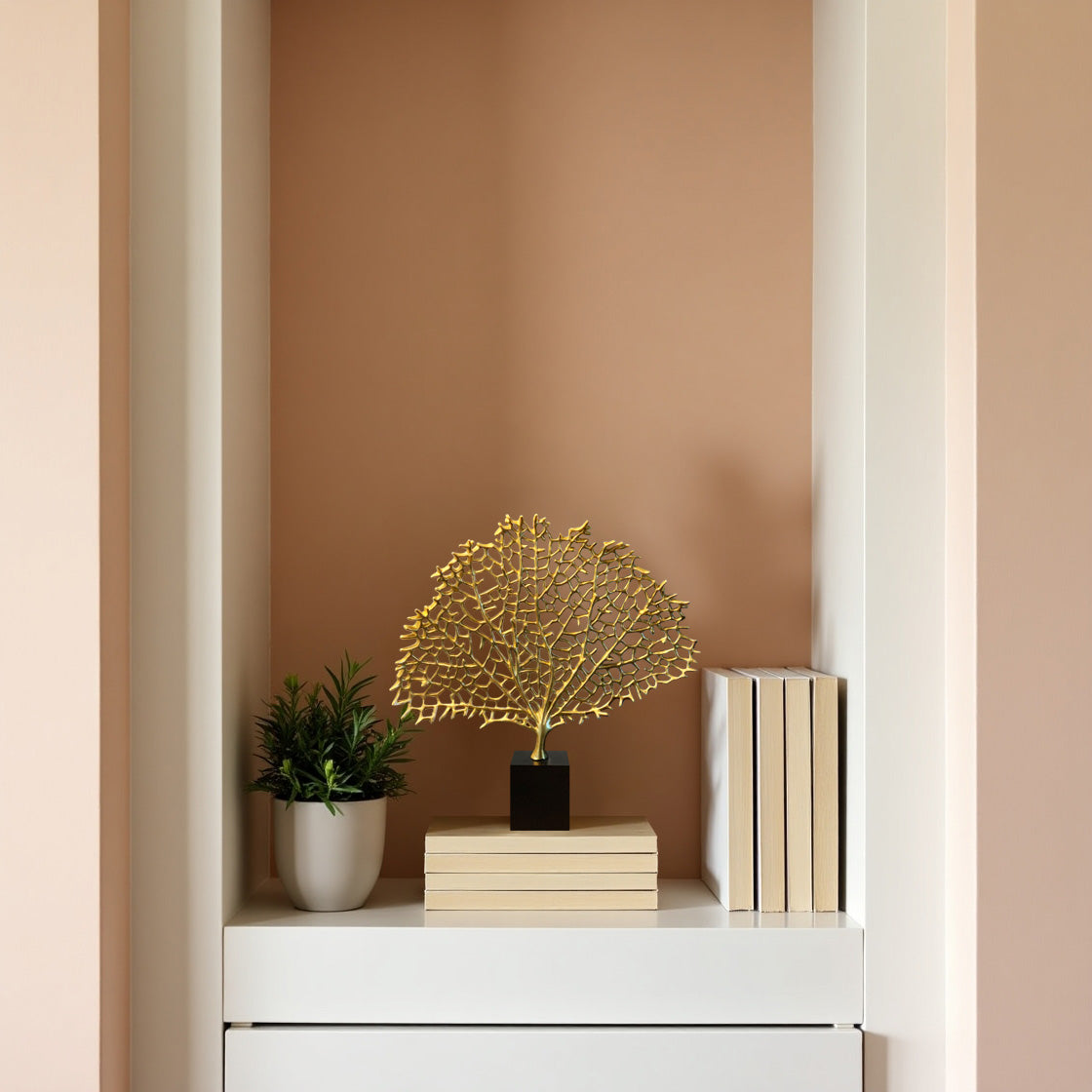 a white shelf with a decorative plant, a small golden sculpture, and a stack of books.