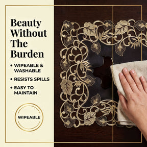 a hand cleaning a decorative table runner with a gold floral pattern. The text highlights the table runner as "Beauty Without The Burden", emphasizing its wipeable and washable nature, as well as its resistance to spills and easy maintenance.
