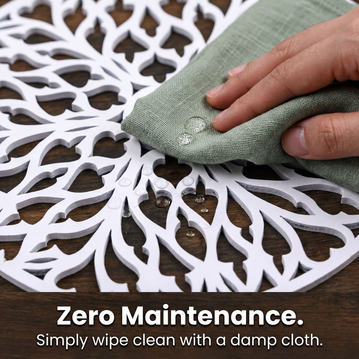 A hand is wiping a white, intricately designed table mat with a damp cloth, as indicated by the text "Zero Maintenance. Simply wipe clean with a damp cloth."
