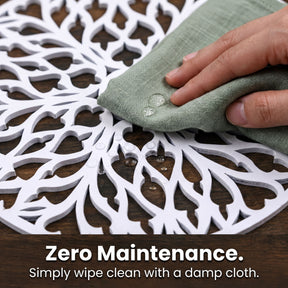 A hand is wiping a white, intricately designed table mat with a damp cloth, as indicated by the text "Zero Maintenance. Simply wipe clean with a damp cloth."