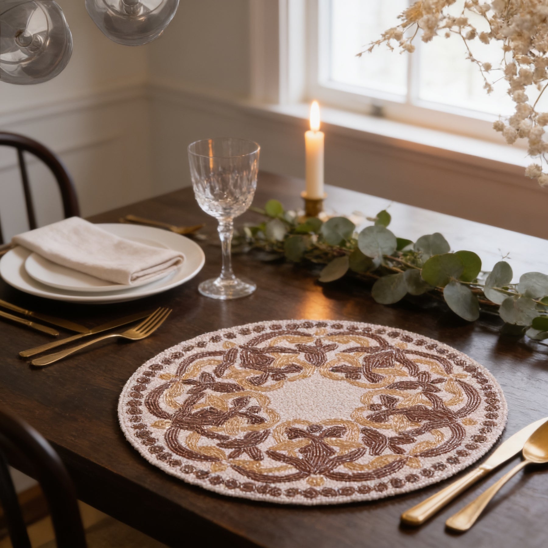 a beautifully set dining table with a white plate, a glass of wine, a candle, and a decorative placemat. The table is set for a meal, with a fork, knife, and spoon placed neatly beside the plate. The overall scene conveys a sense of elegance and sophistication.