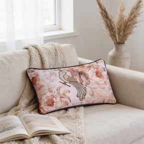 a cozy living room scene with a beige sofa, a floral throw pillow, and a vase of dried flowers. There is also an open book on the sofa, suggesting a relaxing and comfortable atmosphere.