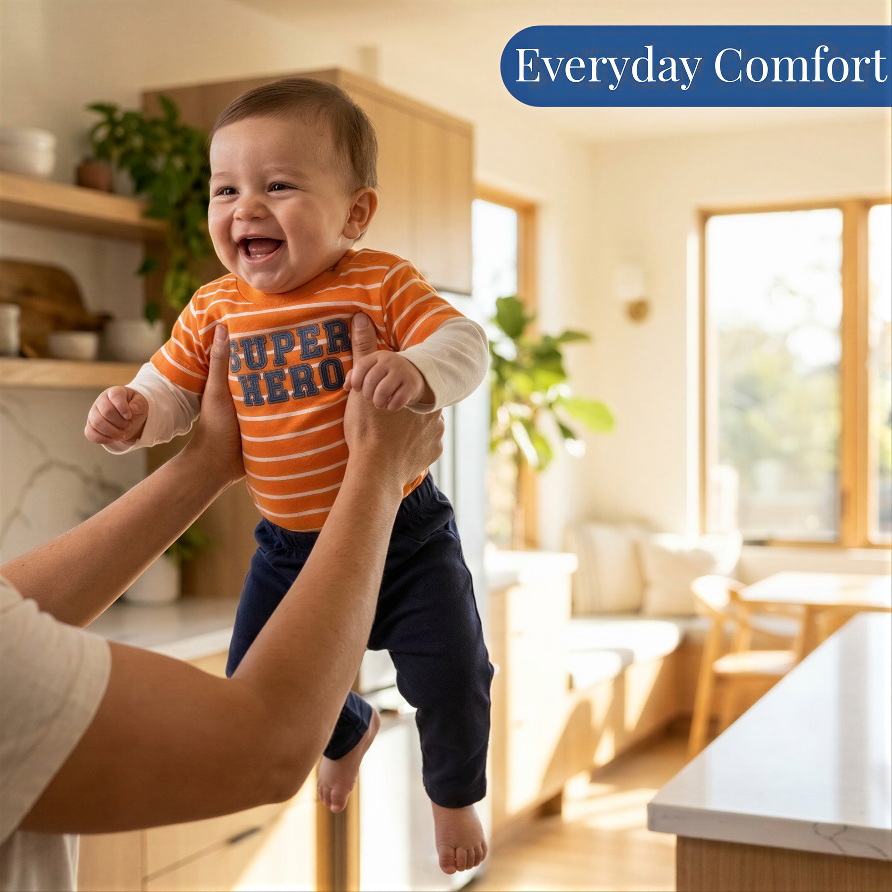 A smiling baby wearing an orange and blue striped shirt is being held up by someone in a kitchen.
