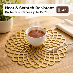 A white mug filled with a steaming beverage sits on a gold, circular placemat on a wooden table.