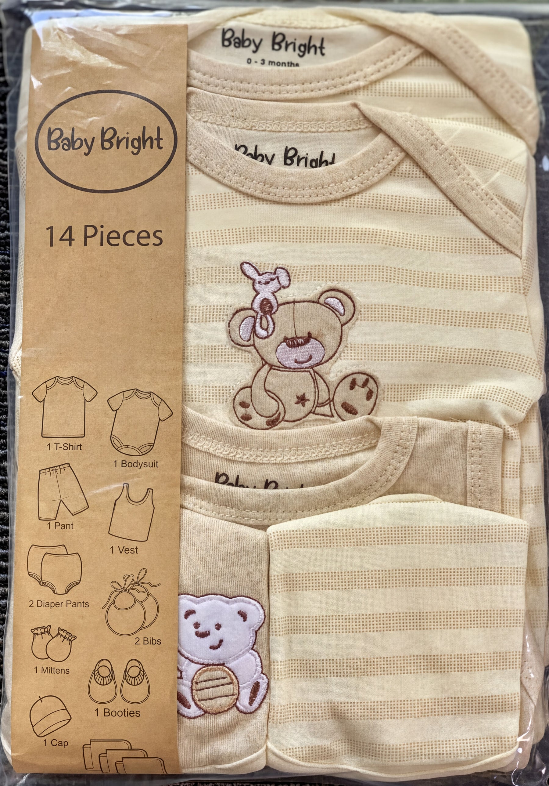 A package containing a set of baby clothing items, including a t-shirt, bodysuit, pants, and booties, with a teddy bear design on the clothing.