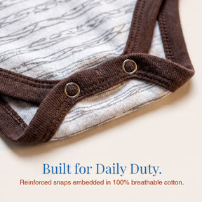 A close-up view of a baby onesie with a brown fabric trim and a white patterned fabric overlay.