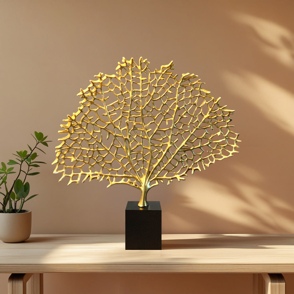 a decorative golden sculpture of a tree or plant, placed on a black pedestal or base, which is situated on a wooden table.