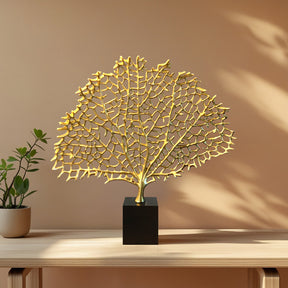 a decorative golden sculpture of a tree or plant, placed on a black pedestal or base, which is situated on a wooden table.