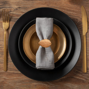 A black plate with a gold rim, a gray napkin ring, and a gold fork and knife are arranged on a wooden table.